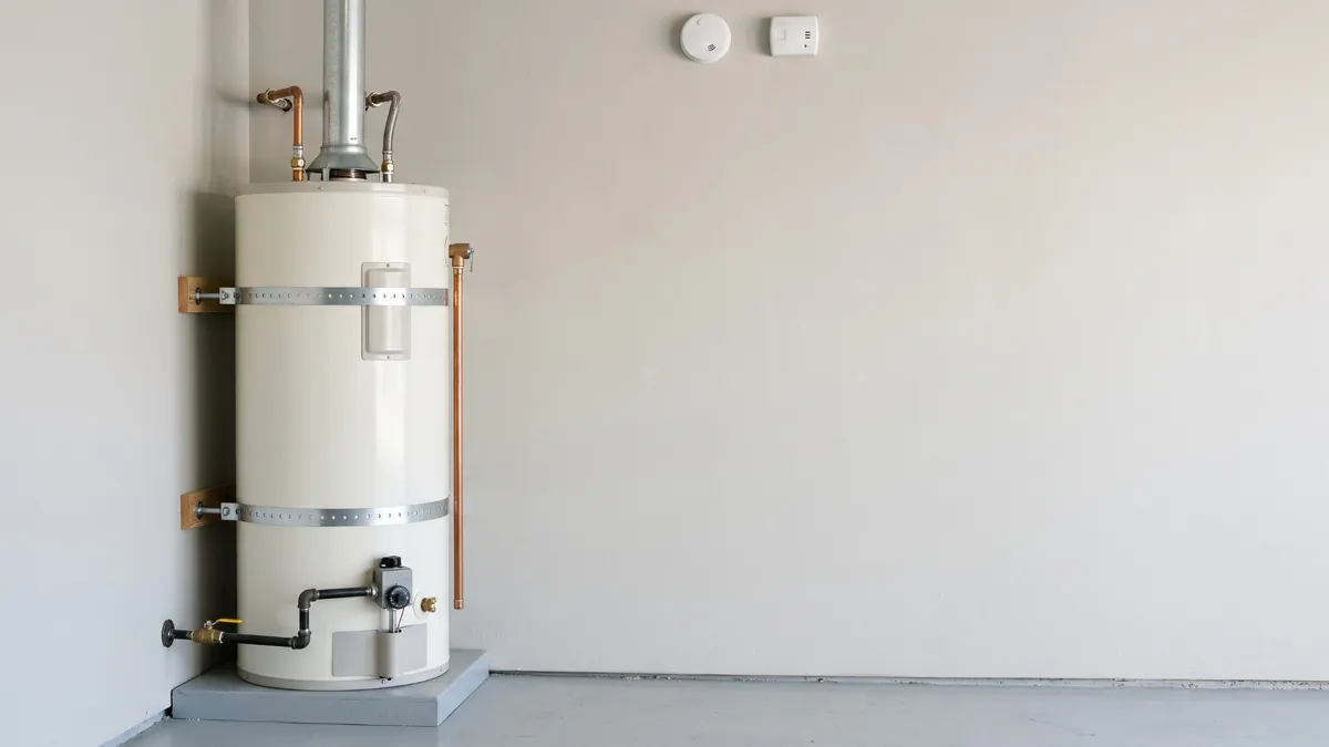 A gas water heater in a garage with two steel earthquake straps fastened to the wall, and smoke and carbon monoxide alarms nearby
